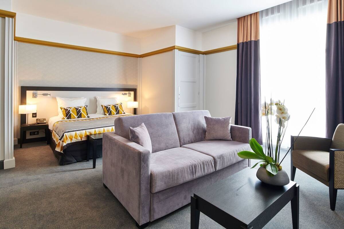 A hotel room with a bed, a sofa, a coffee table, and a potted plant.