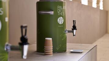Un bote verde para basura con un grifo y una pila de vasos de papel, con la etiqueta 'Palais des Thés Paris'.
