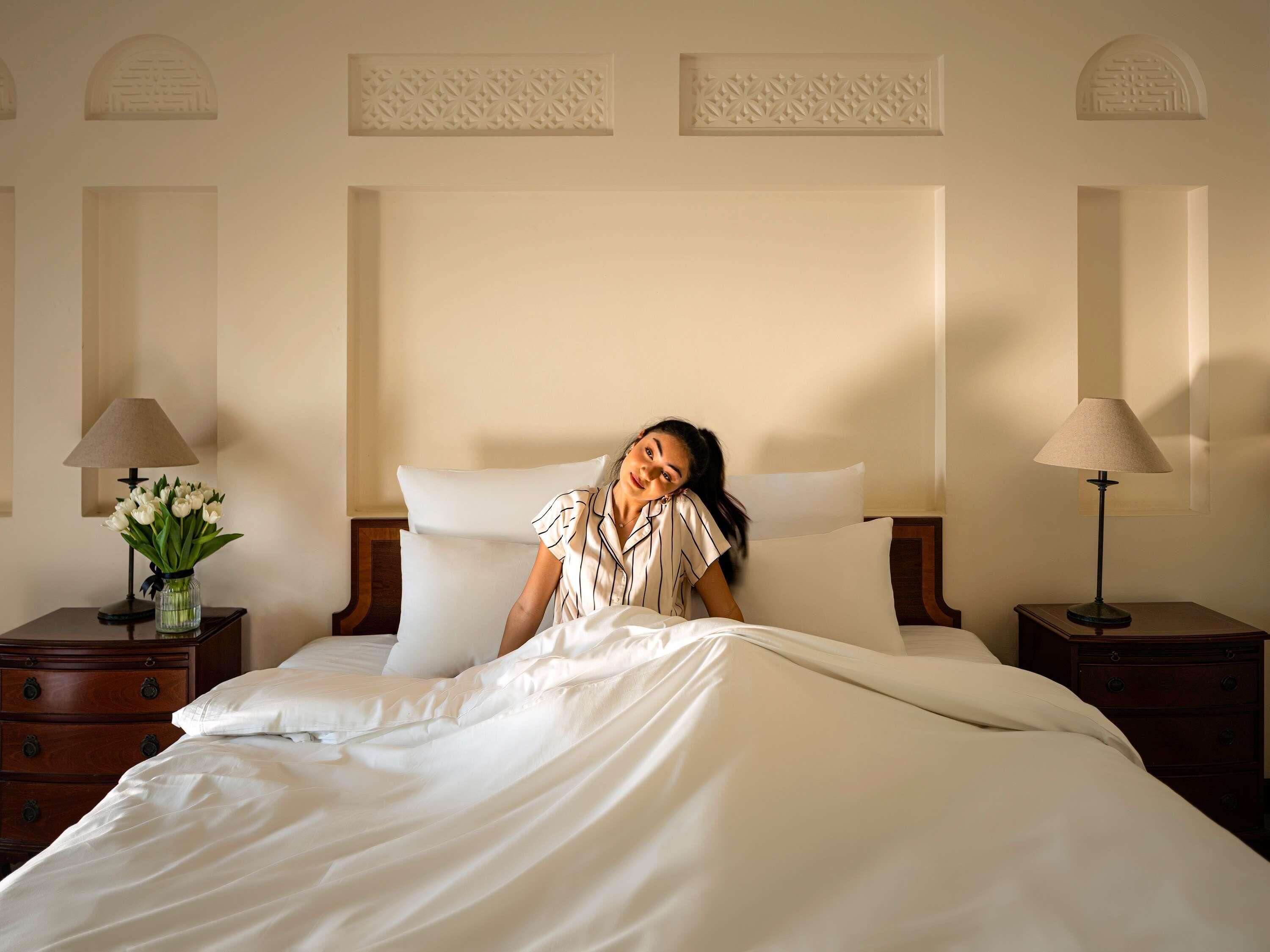 A hotel room with a bed, two nightstands, a vase with flowers, and a decorative wall panel.