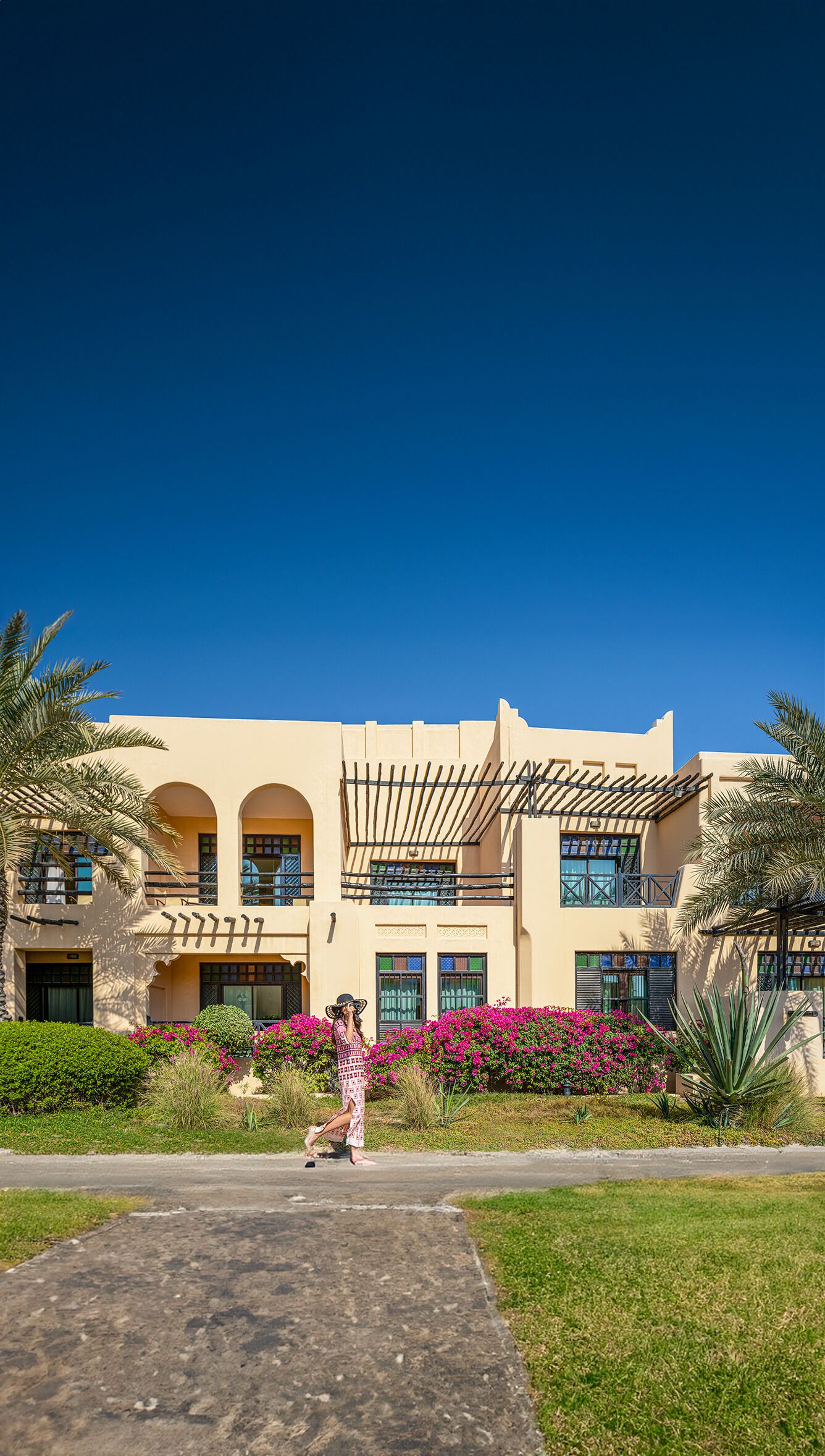 Un edificio con fachada color beige, varias ventanas y un espacio exterior cubierto con una pérgola.