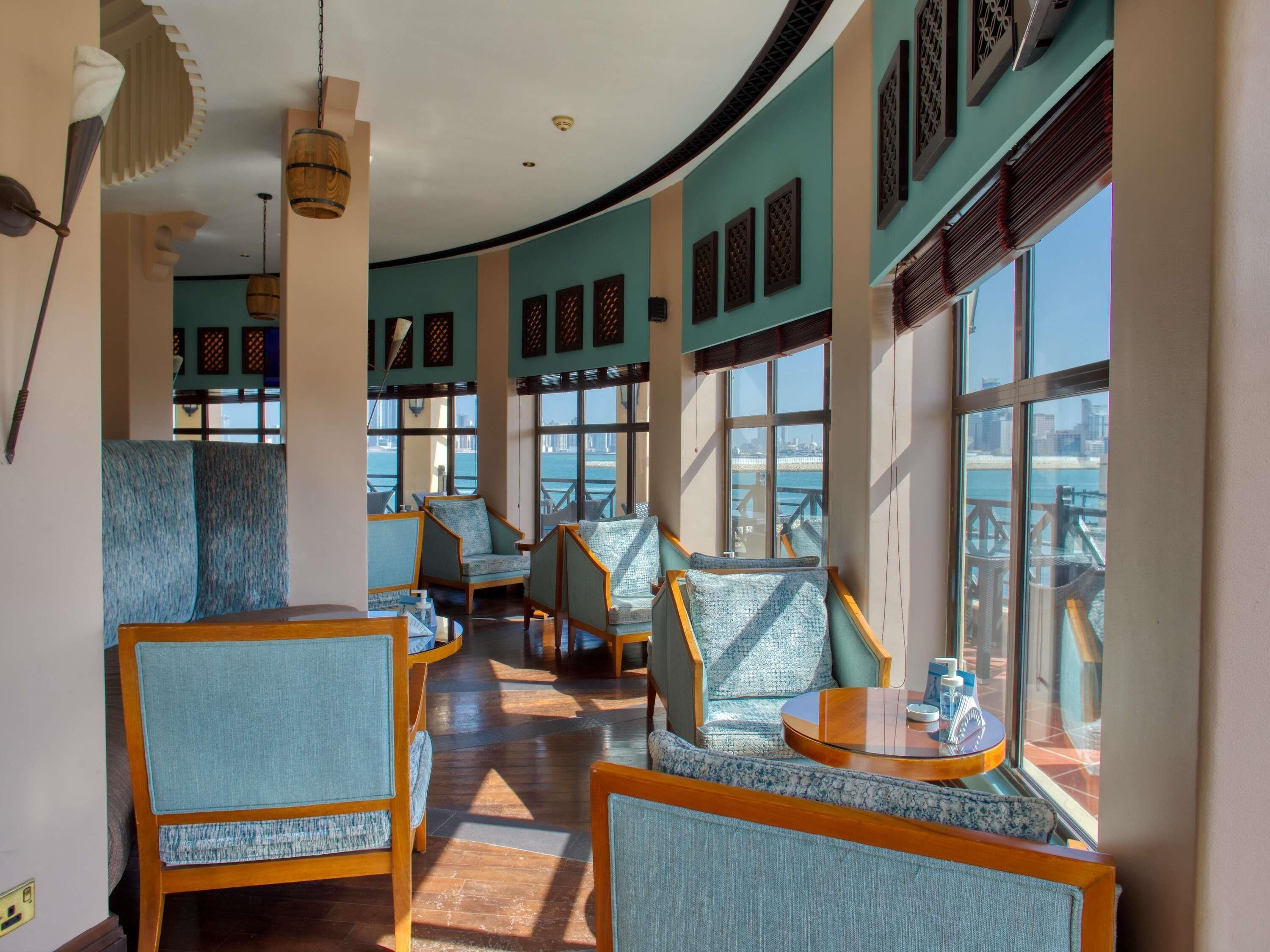 Un vestíbulo de hotel con asientos, ventanas amplias y vistas del horizonte urbano.