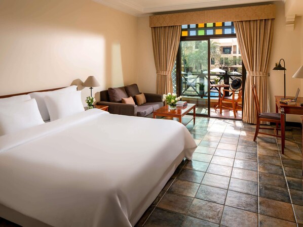 Habitación de hotel con una cama grande, un sofá, una mesa de centro, un escritorio y vistas al exterior.
