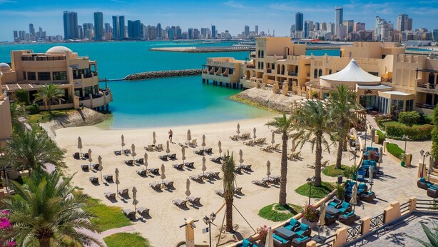 A resort with a beachfront, palm trees, and a city skyline in the background. - Novotel Bahrain Al Dana Resort (Manama)