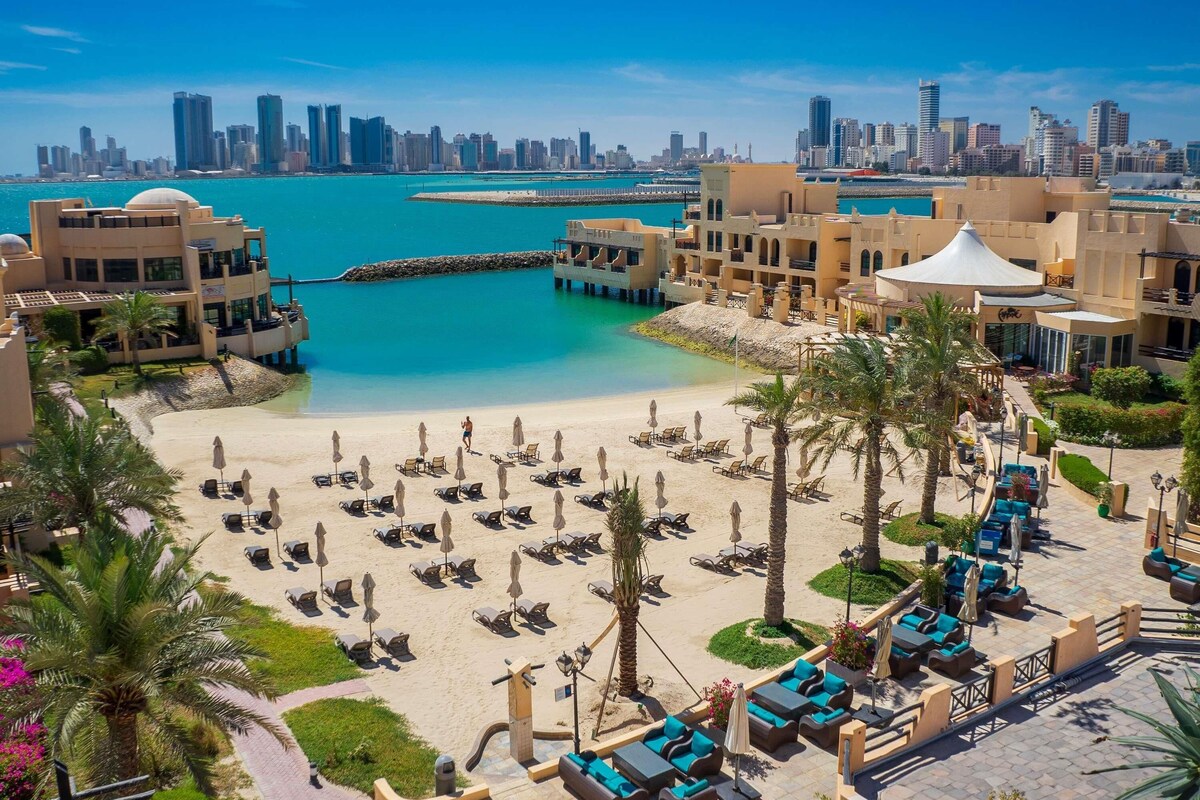 A resort with a beachfront, palm trees, and a city skyline in the background.