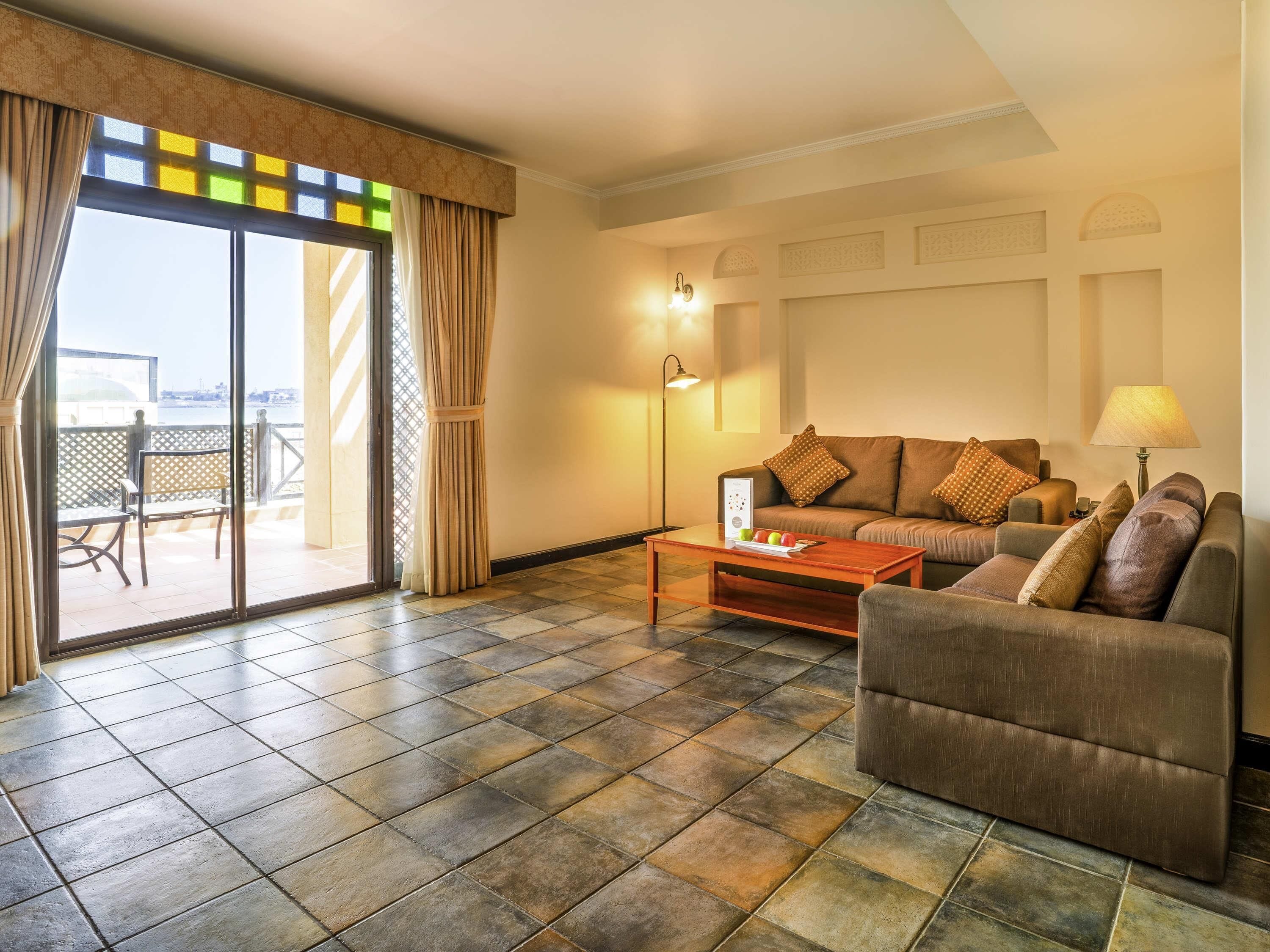 A living room with a sofa, armchair, and a coffee table. There is a sliding glass door leading to an outdoor area with a view.