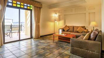 Uma sala de estar com sofá, poltrona e mesa de centro. Há uma porta de vidro deslizante que dá para uma área externa com vista.