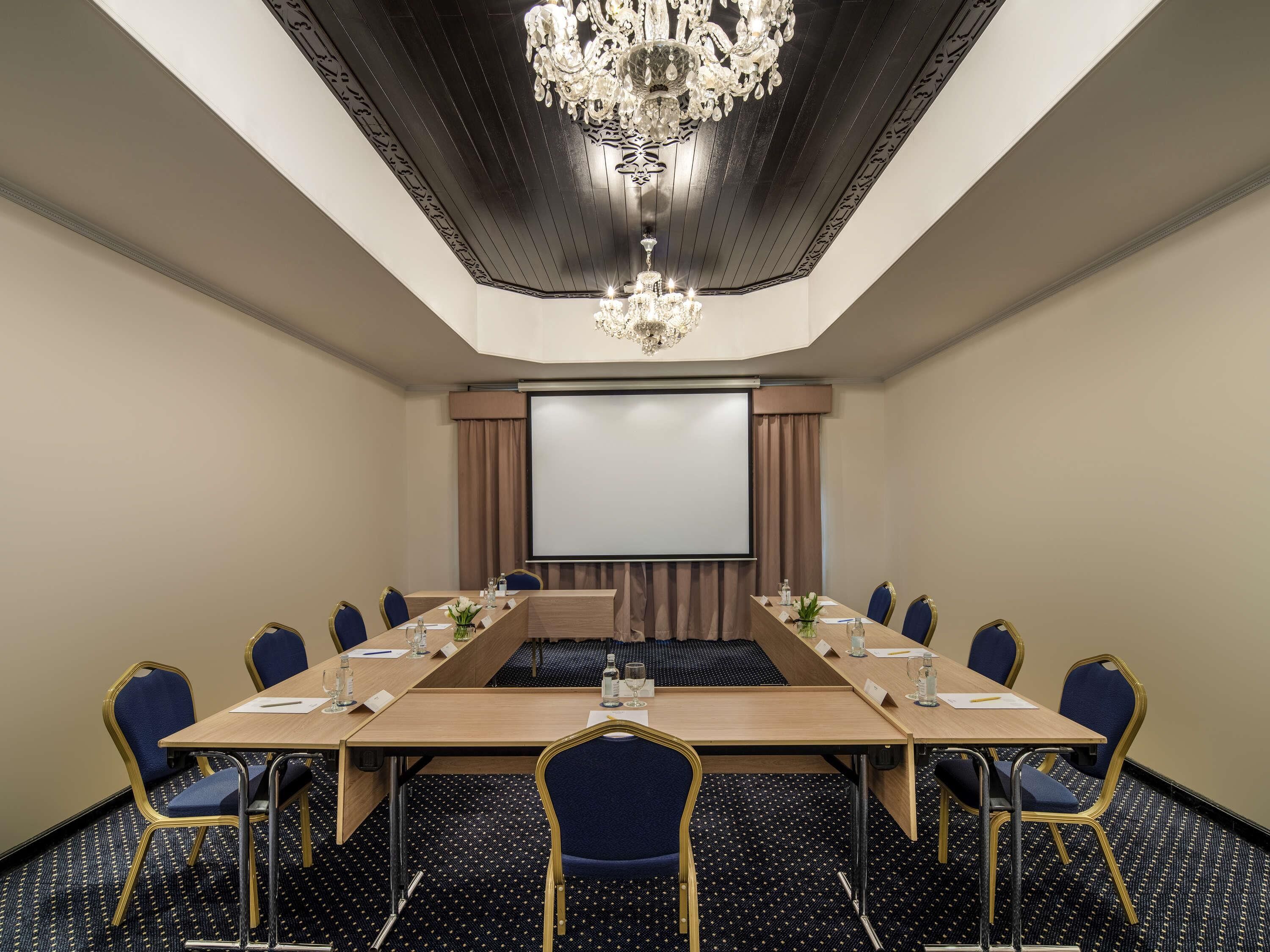 A conference room with a long table, chairs, a projector screen, and a chandelier.