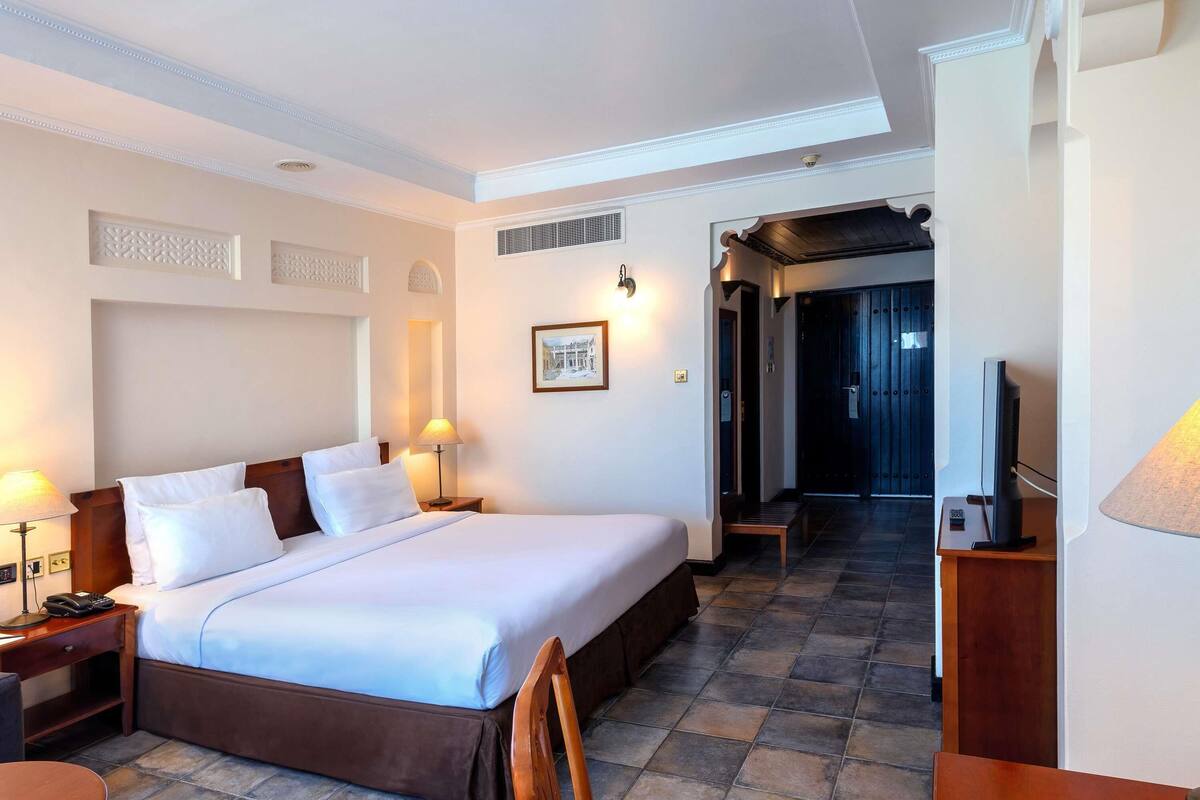 A hotel room with a large bed, bedside tables, a desk, and a television.