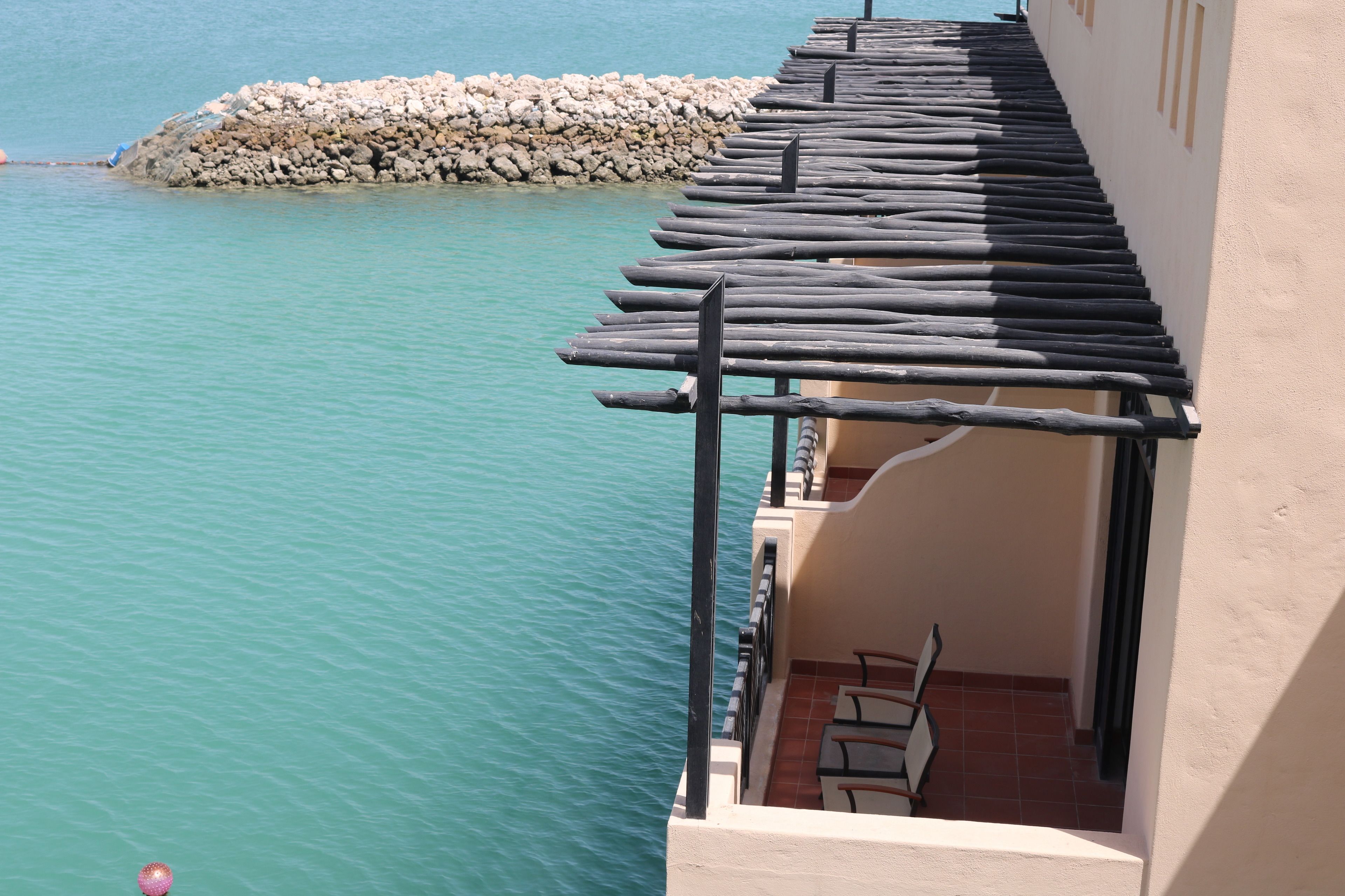 A balcony with a view of turquoise water and a rocky breakwater.
