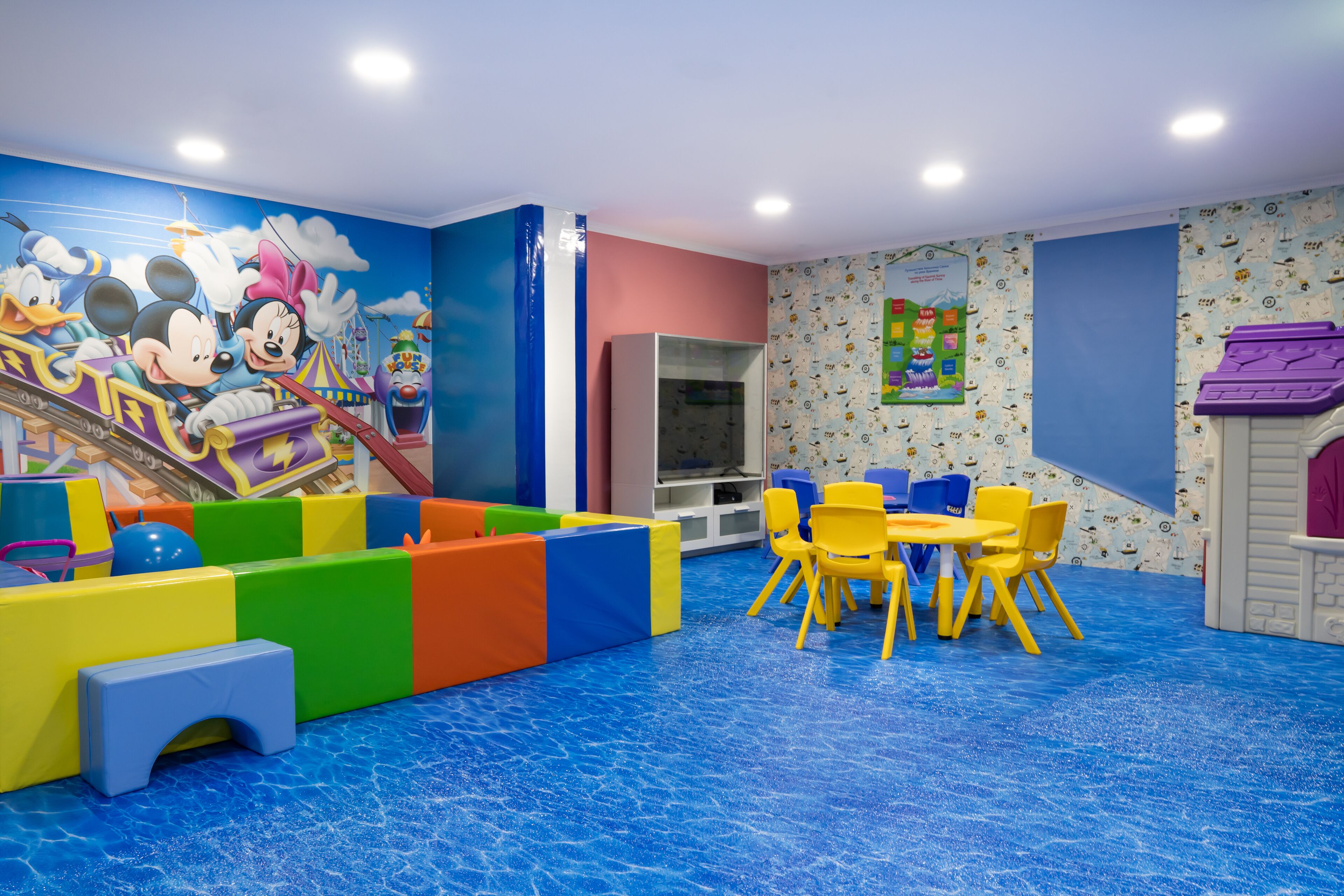 Uma área de recreação infantil com estruturas coloridas, um escorrega e uma mesa com cadeiras.