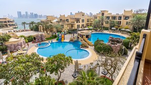 A resort with a central swimming pool, palm trees, and a view of the city skyline. - Novotel Bahrain Al Dana Resort (Manama)
