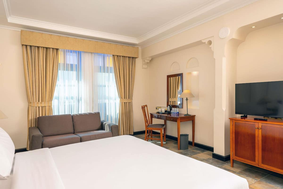 A hotel room with a large bed, a sofa, a desk with a chair, a television, and curtains.