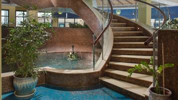Una piscina interior moderna con una escalera de cristal y plantas en macetas.