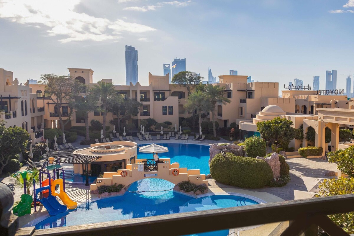 A resort with a swimming pool, lounge chairs, and palm trees.
