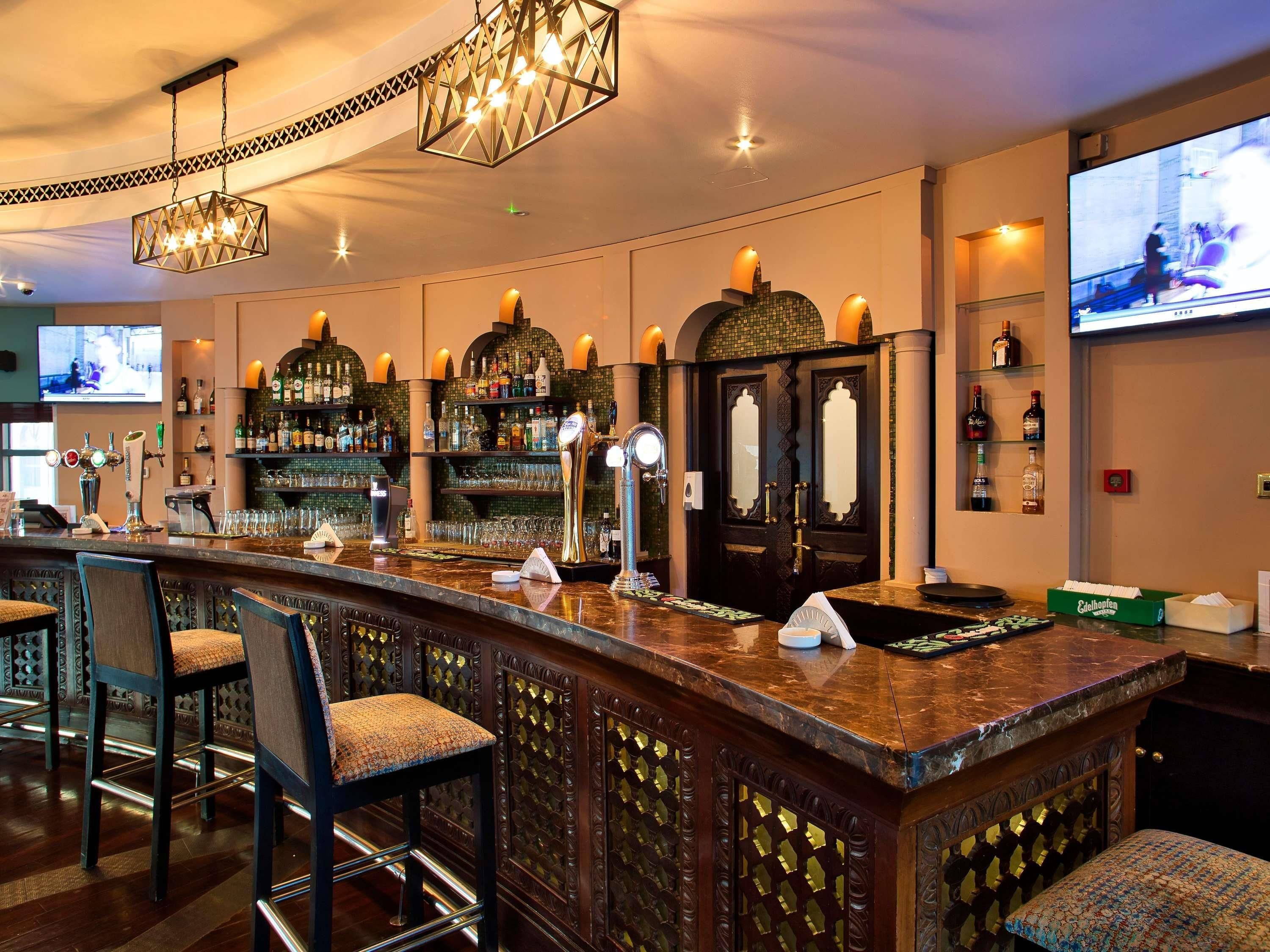 A bar area with a counter, bar stools, a television screen, and a decorative ceiling light.