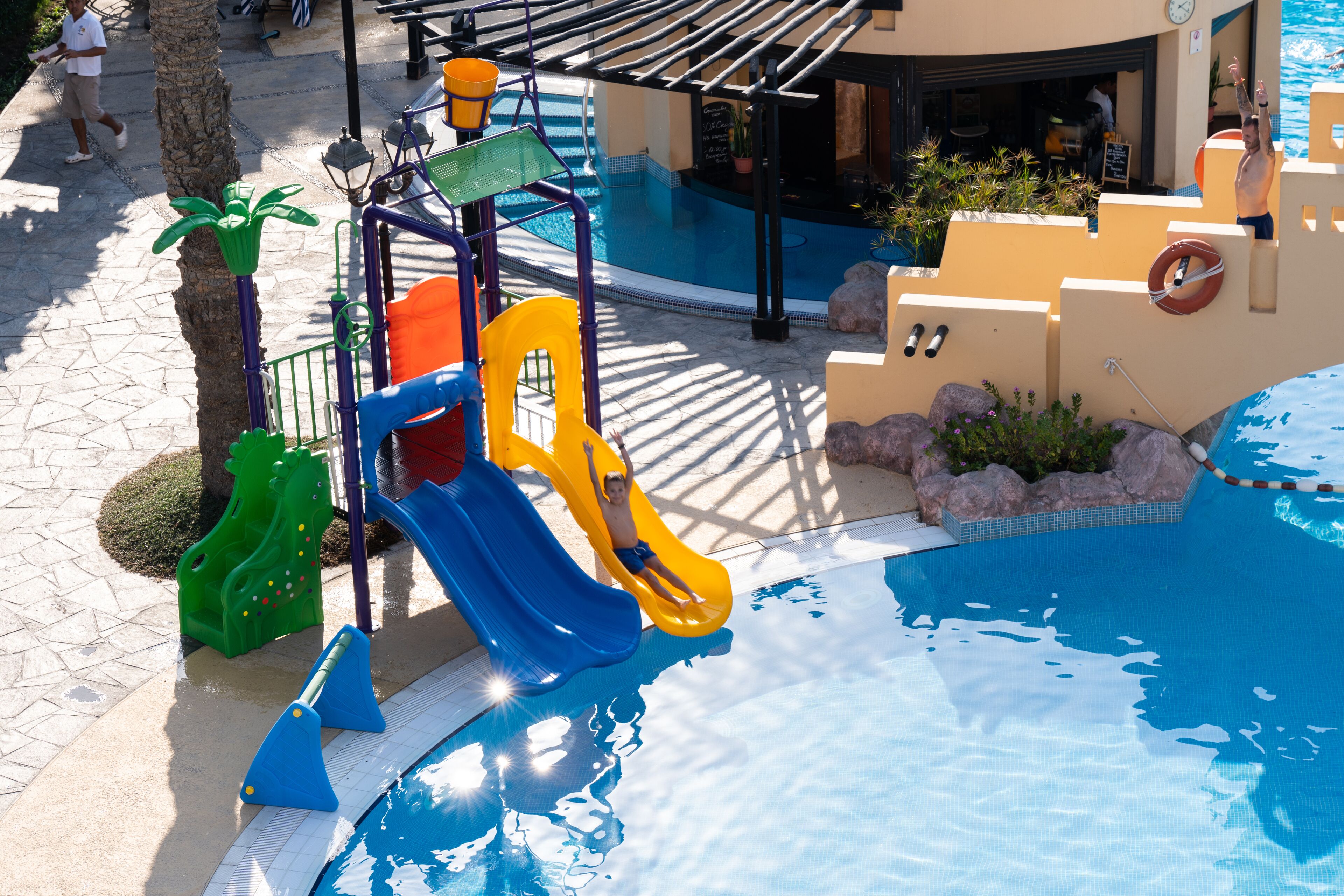 A pool area with a slide, a lifebuoy, and a palm tree.