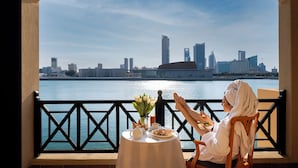 A balcony with a table set for breakfast, overlooking a city skyline and water. - Novotel Bahrain Al Dana Resort (Manama)