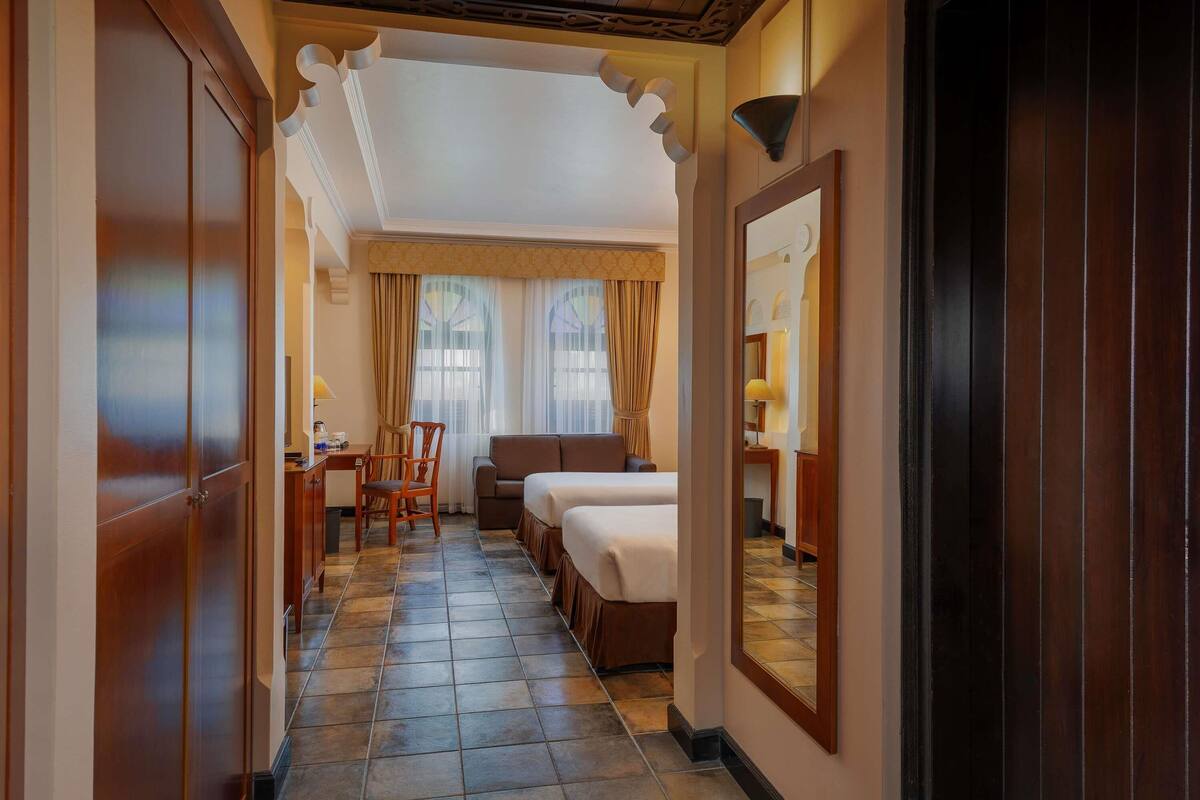 A hotel room with a bed, a desk, a chair, and a large mirror.