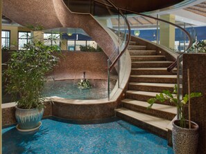 A spiral staircase with a pool at the base, surrounded by tiled walls and potted plants. - Novotel Bahrain Al Dana Resort (Manama)
