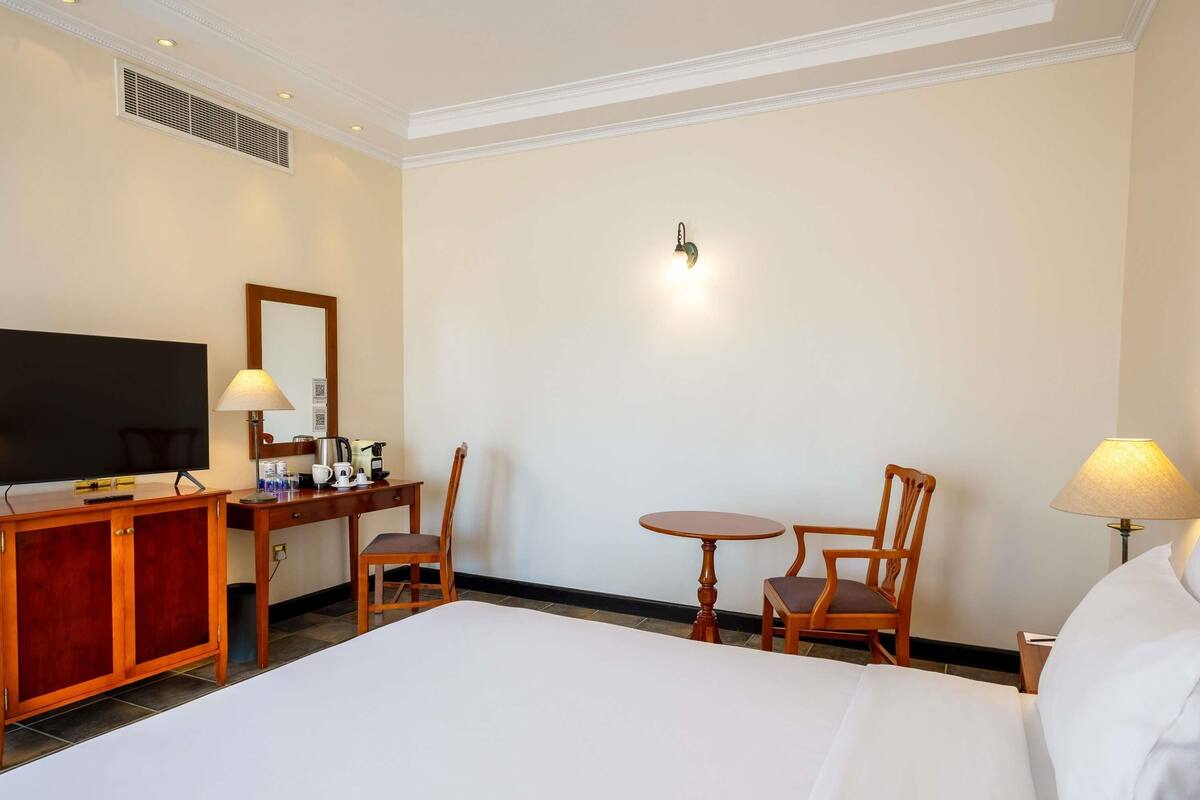 Habitación de hotel con cama, escritorio con televisor, silla, mesita y lámpara.
