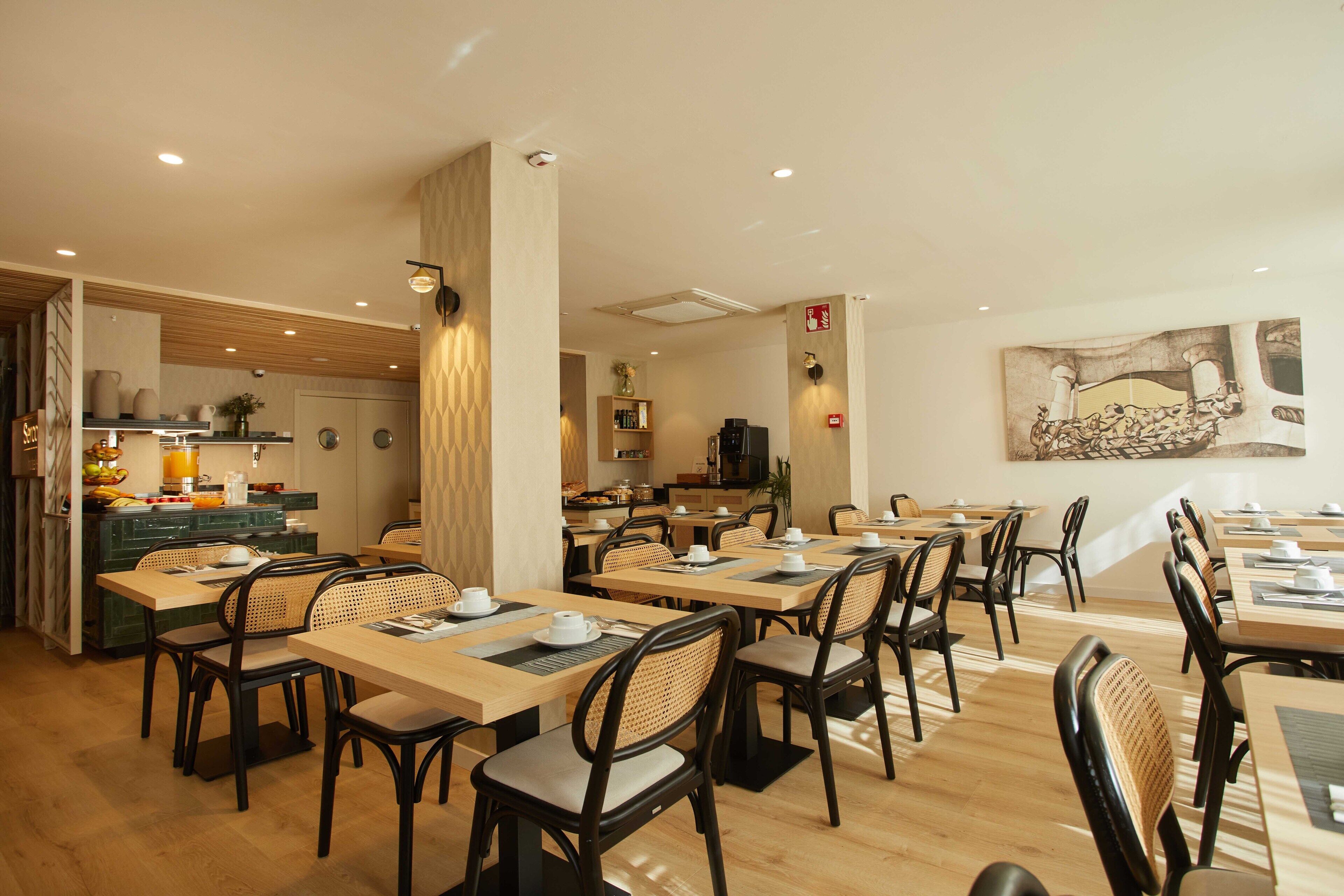 Un restaurante moderno con varias mesas y sillas, una zona de cocina y un elemento decorativo en la pared.