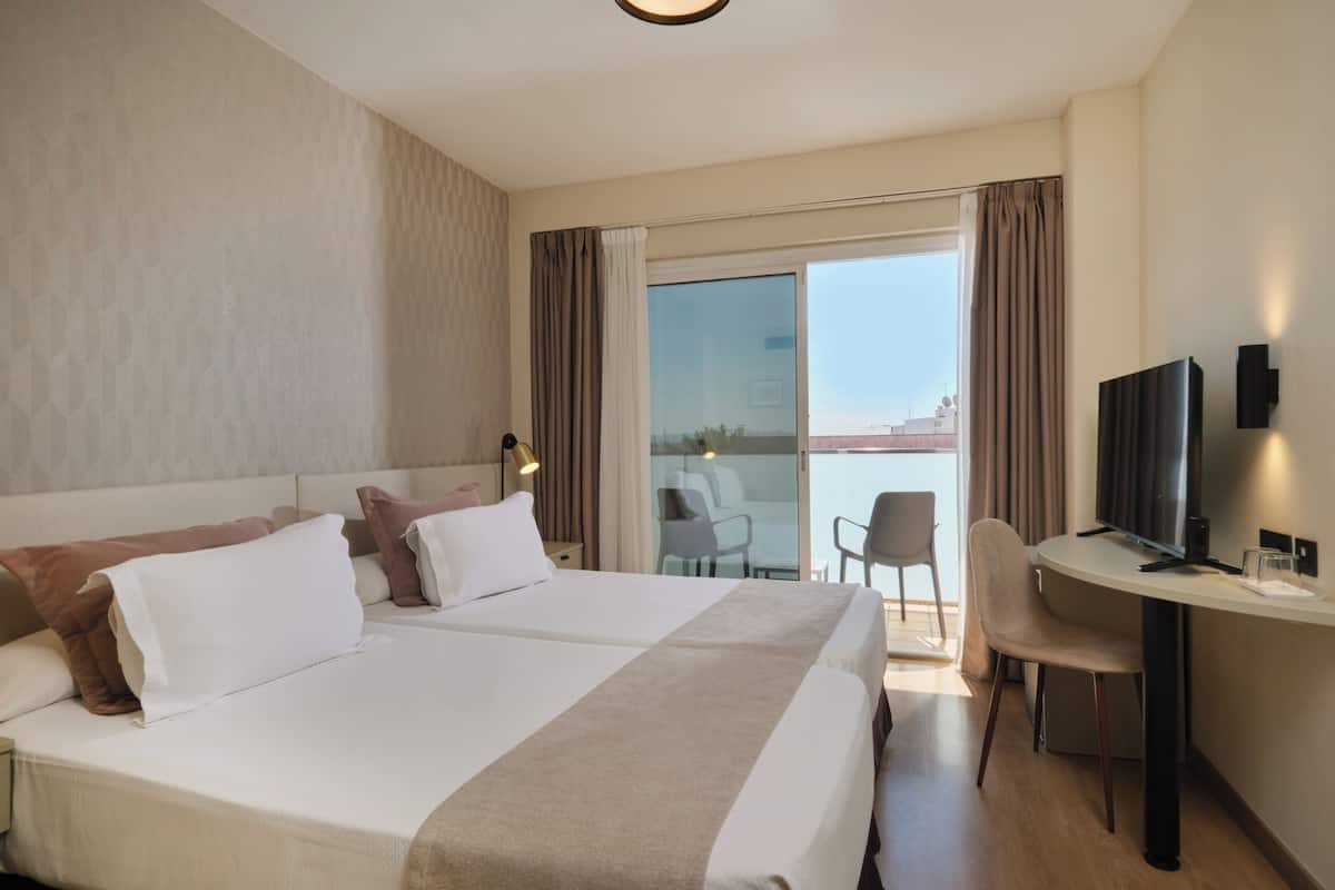 Een hotelkamer met een groot bed, een bureau met een televisie en een balkon met uitzicht.