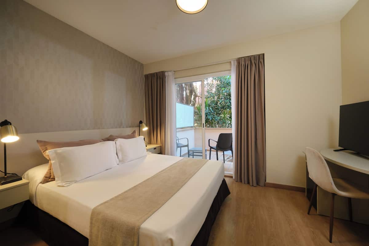 Hotelkamer met een groot bed, een bureau met stoel, een televisie en een balkon met gordijnen.