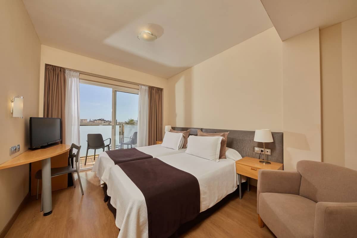 Een hotelkamer met een bed, een bureau met een televisie, een stoel, een nachtkastje met een lamp en uitzicht op het omliggende landschap.