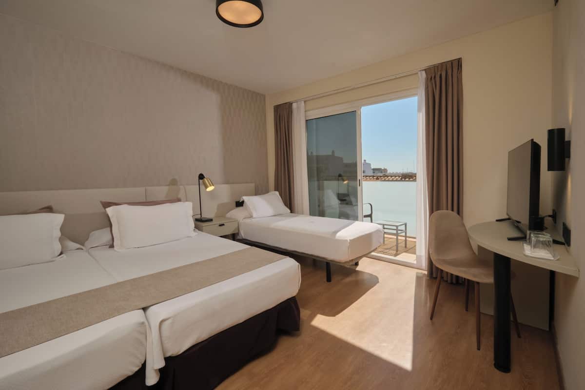 Een hotelkamer met twee bedden, een bureau, een stoel, een televisie en een balkon met uitzicht.
