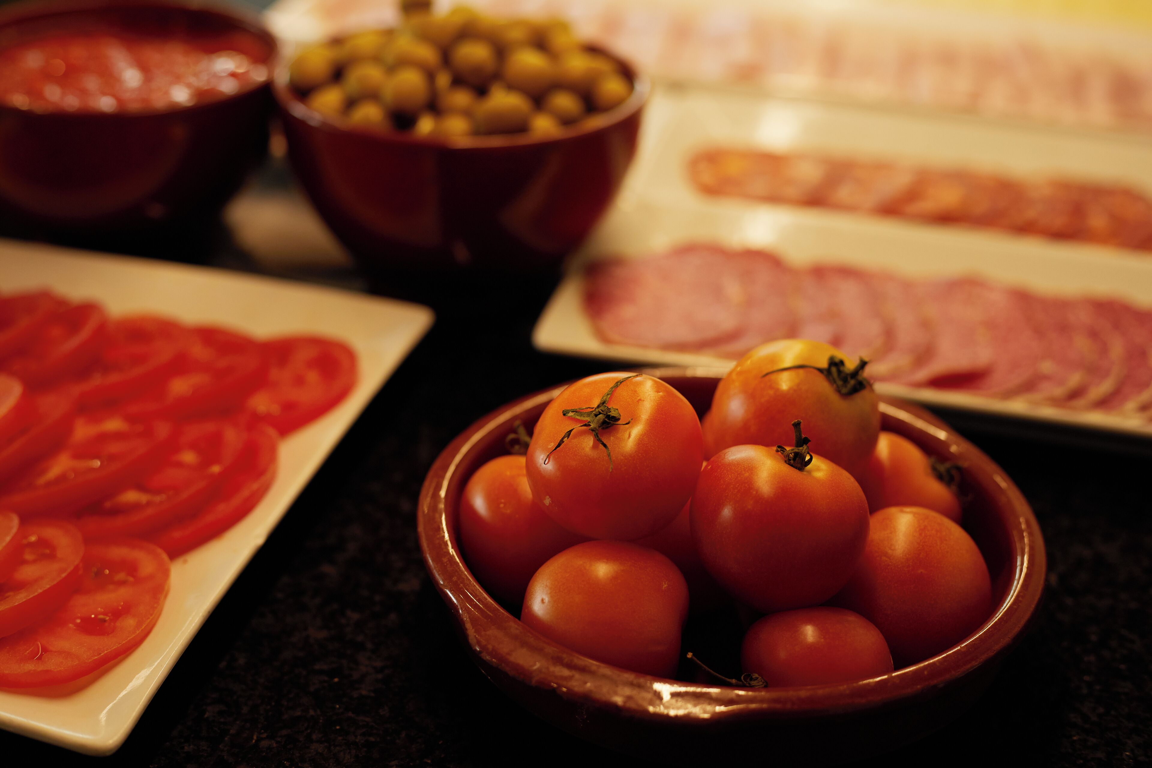 Ein Tisch mit verschiedenen Speisen, darunter Tomaten, Oliven und Aufschnitt.