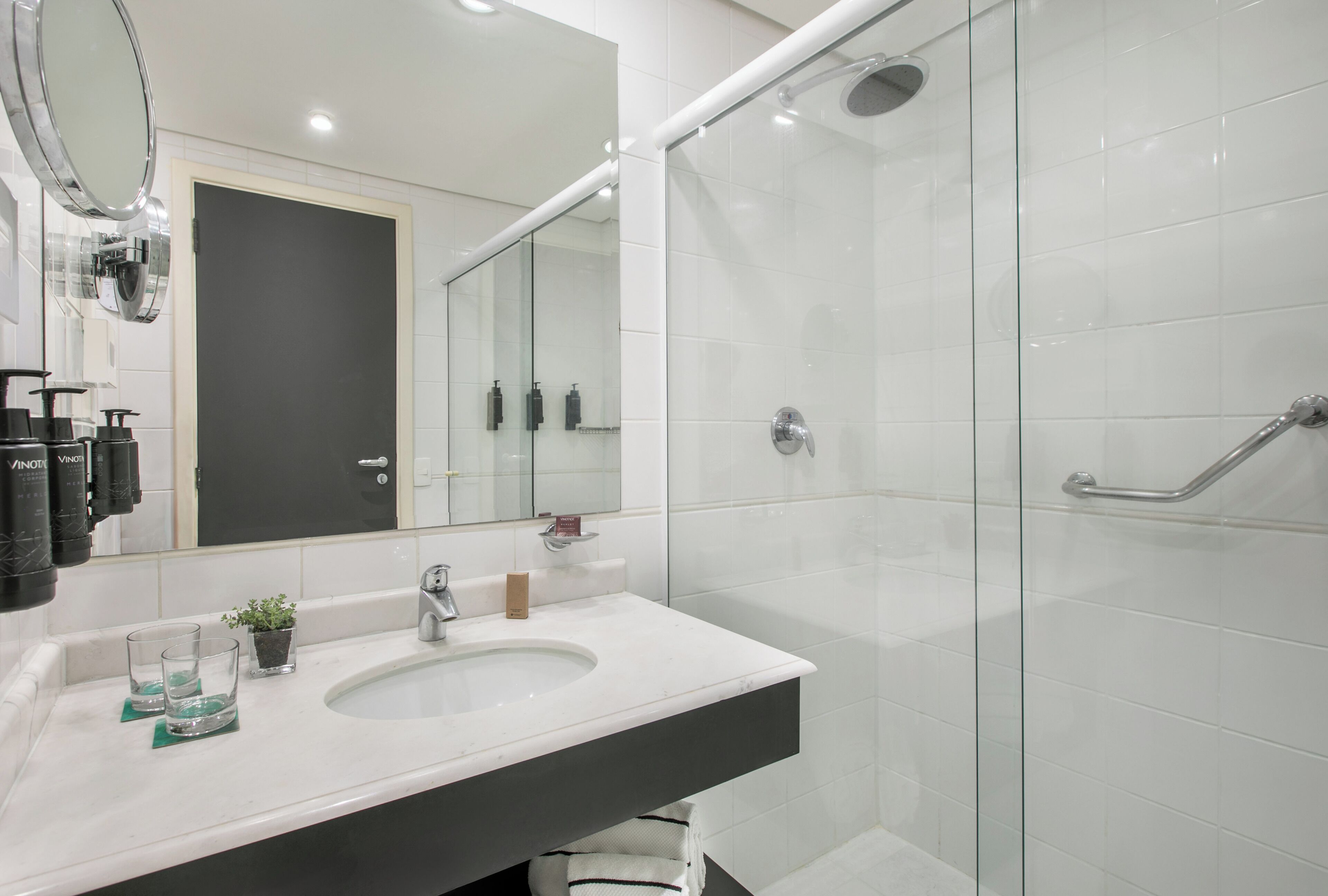 Un baño moderno con un espejo grande, un lavamanos y una ducha con mampara de vidrio.