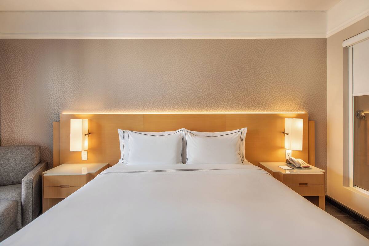Habitación de hotel con una cama grande, dos mesitas de noche, una silla y una mesita con teléfono.