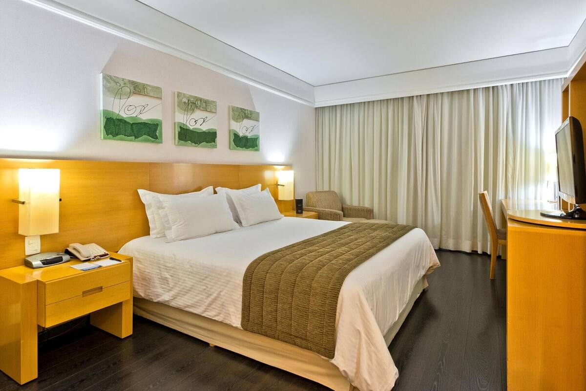 Habitación de hotel con cama, mesitas de noche, un escritorio, una silla, televisor y cortinas.