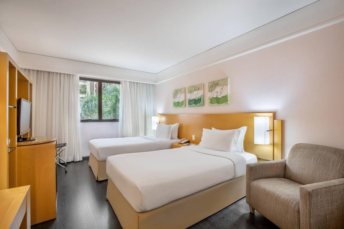Una habitación de hotel con dos camas, un escritorio, una silla y un televisor.