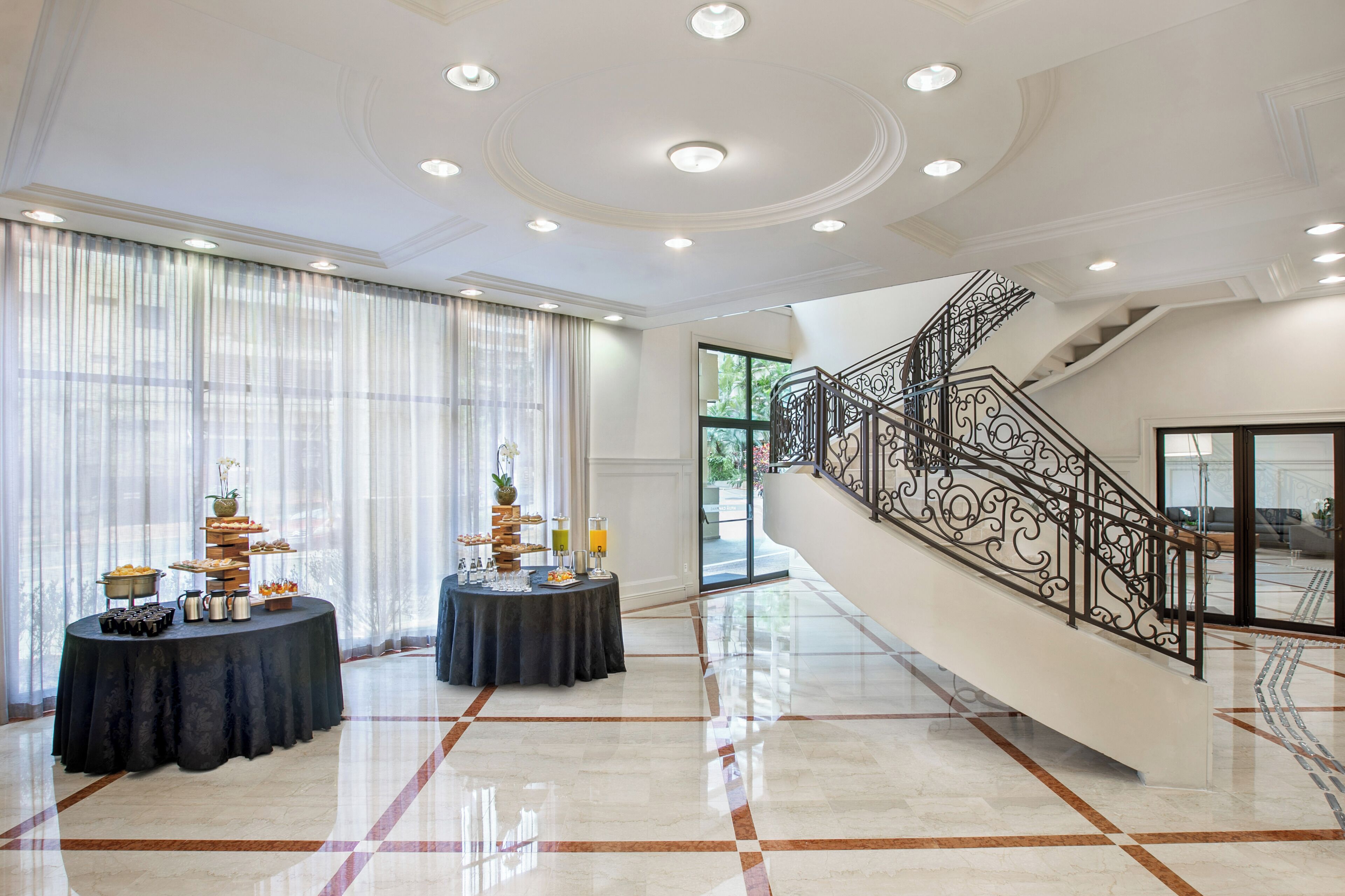 A spacious lobby with a grand staircase, a buffet table, and a large window with sheer curtains.