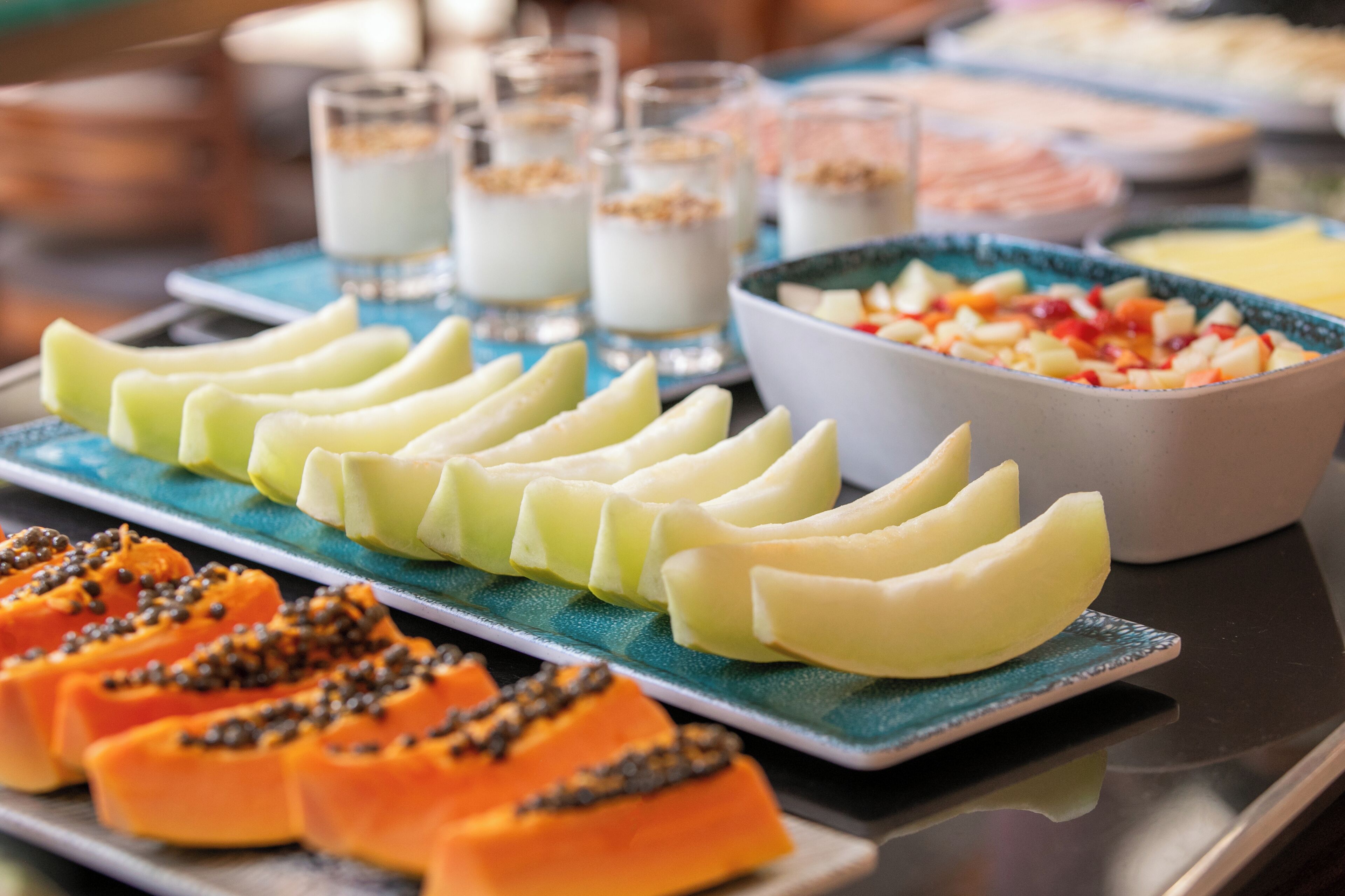 Un bufé con diversas frutas y postres, incluyendo mango en rodajas, papaya y un tazón de ensalada de frutas variadas.