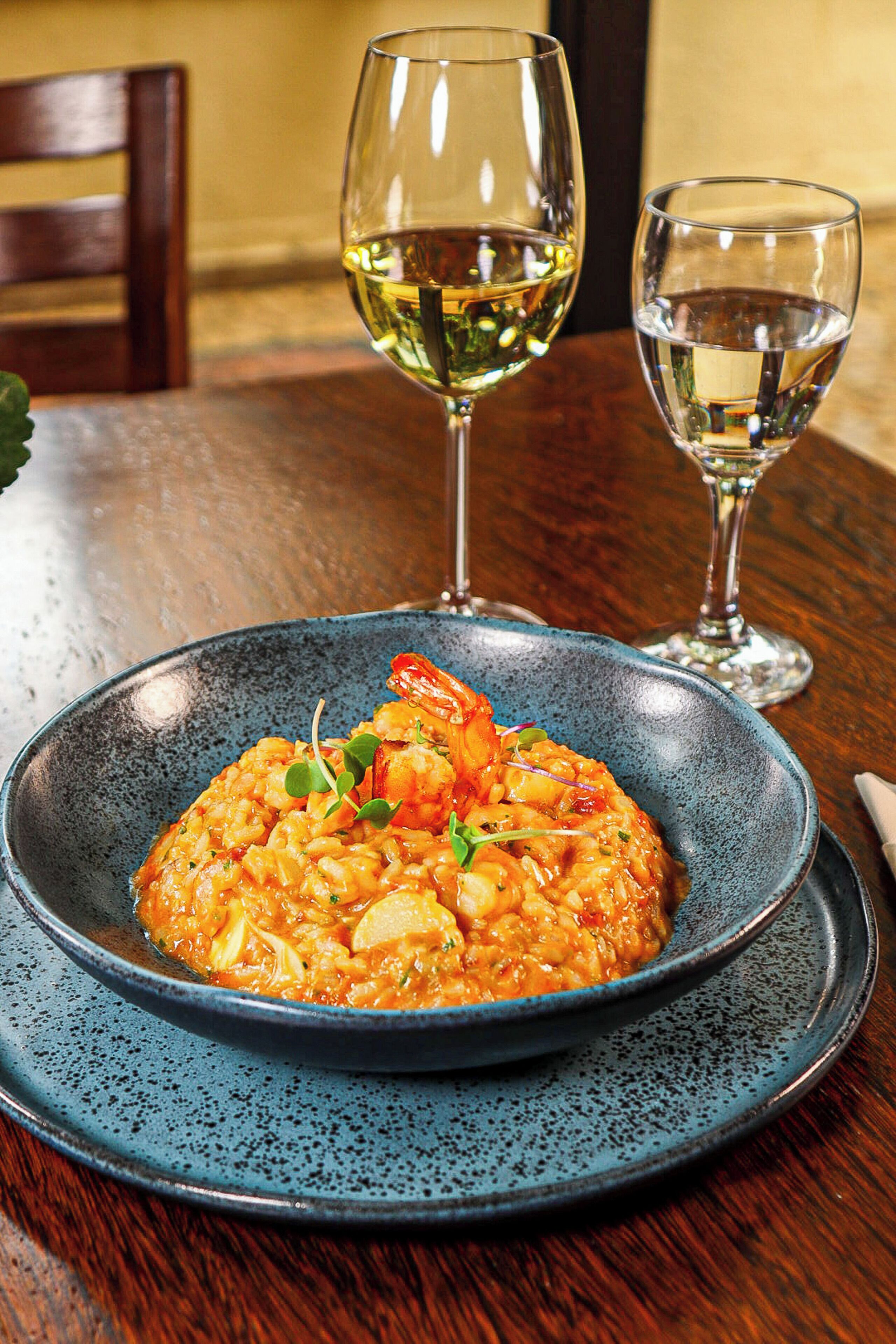 Un piatto di risotto ai frutti di mare con un bicchiere di vino bianco e un bicchiere d'acqua su un tavolo di legno.