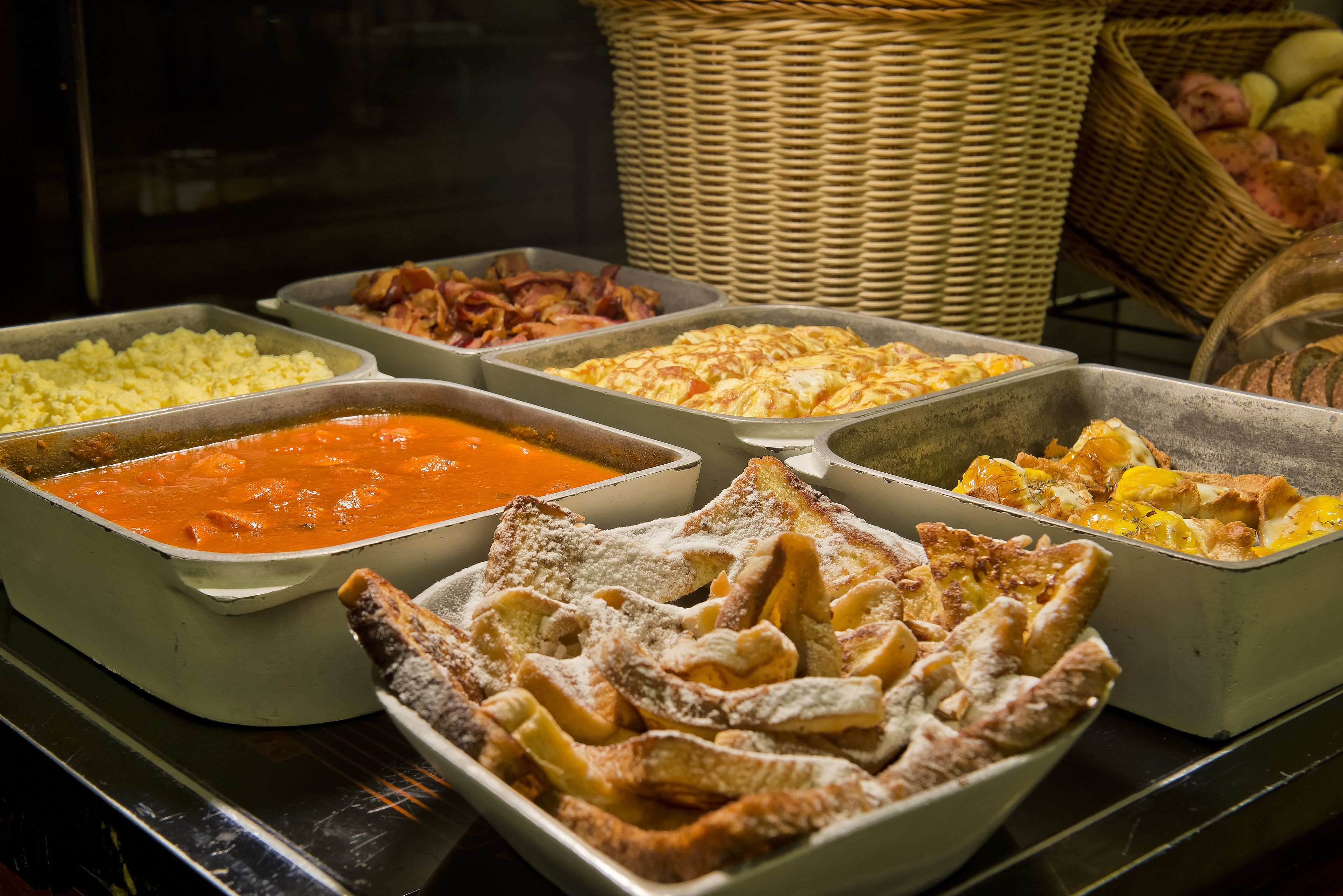 Ein Buffet mit verschiedenen Speisen, darunter Rührei, Speck und einer Auswahl an Soßen.