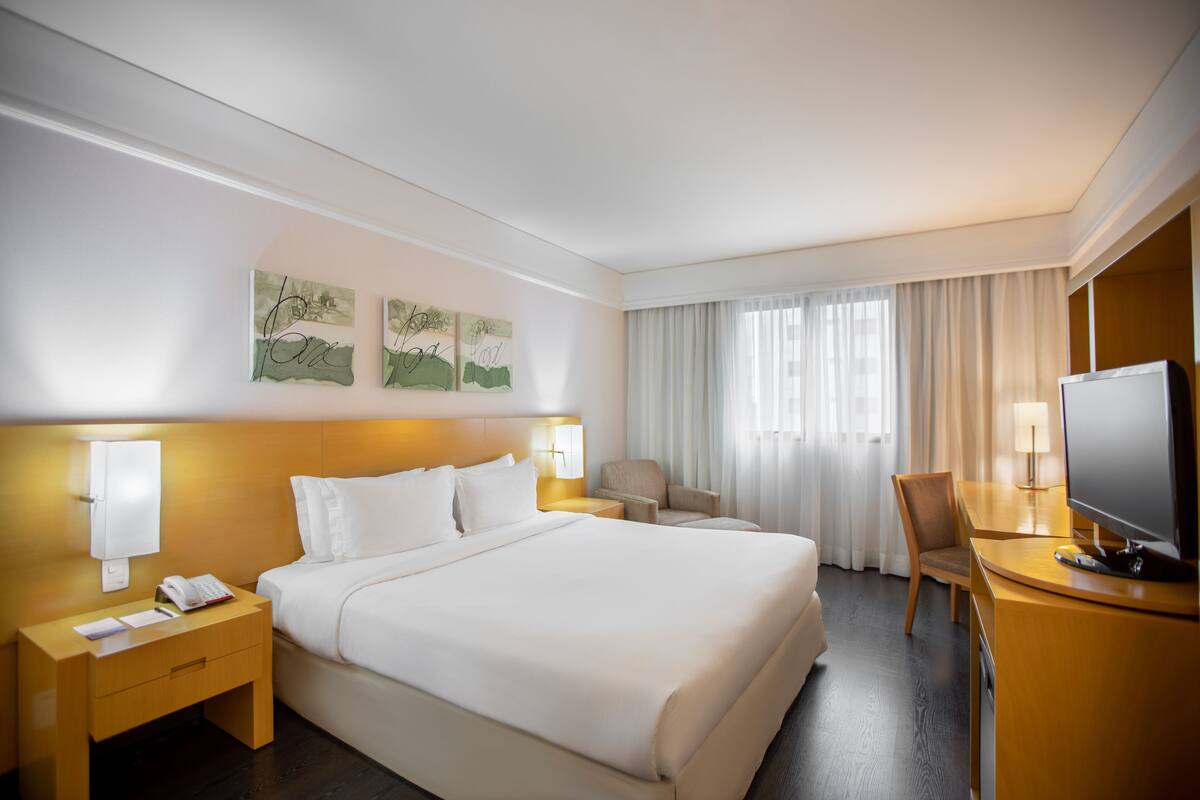 Habitación de hotel con una cama grande, mesitas de noche, un escritorio con televisor y una silla.