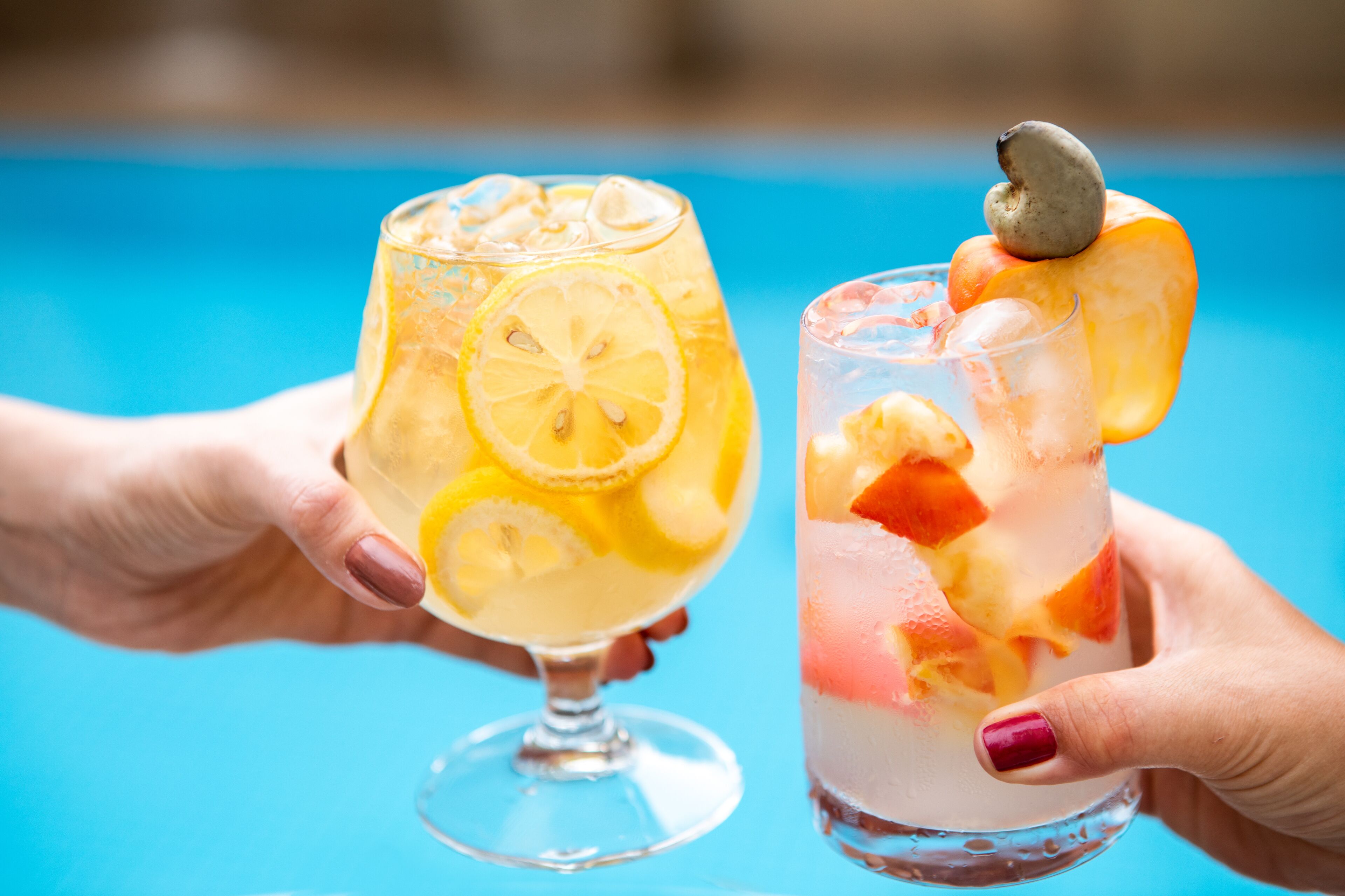 Dos manos sosteniendo vasos de bebidas heladas con rodajas de fruta.