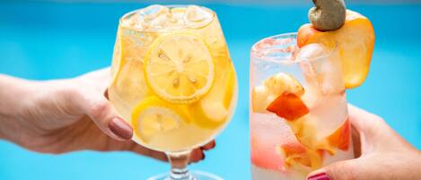 Dos manos sosteniendo vasos de bebidas heladas con rodajas de fruta.