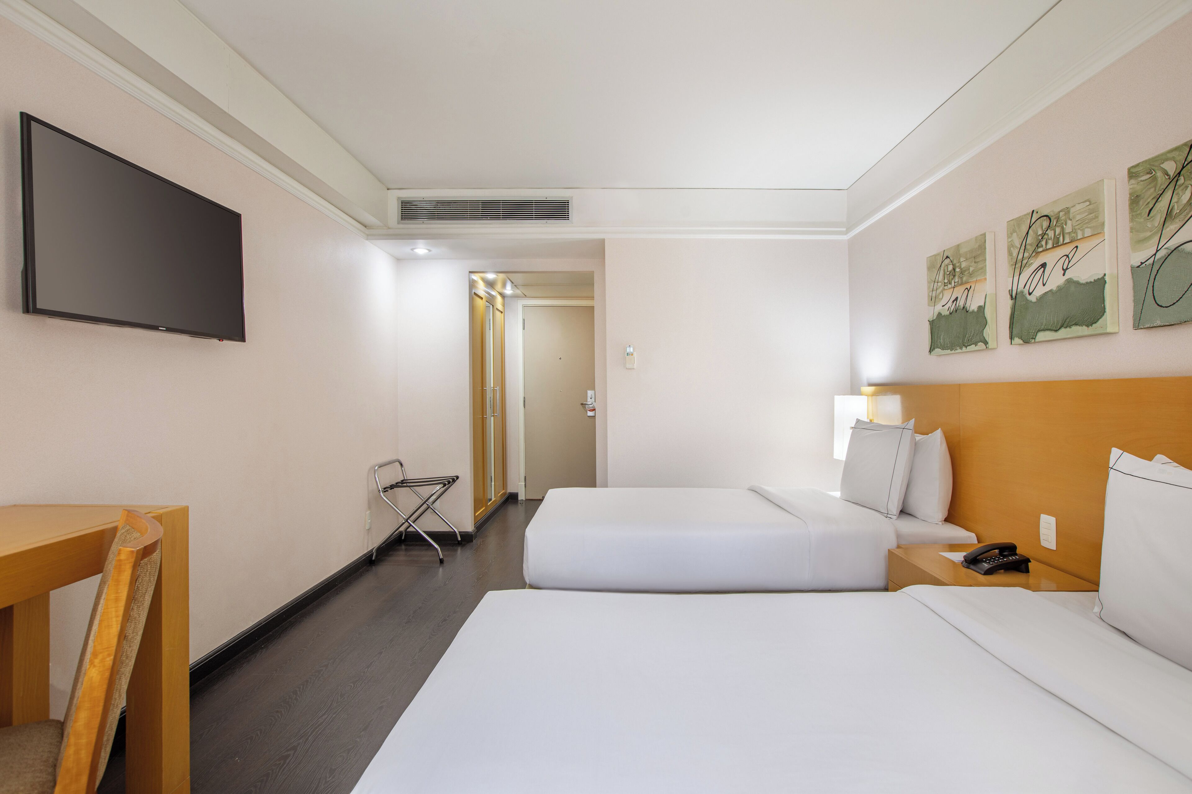 A hotel room with two beds, a TV, a desk, and a chair.
