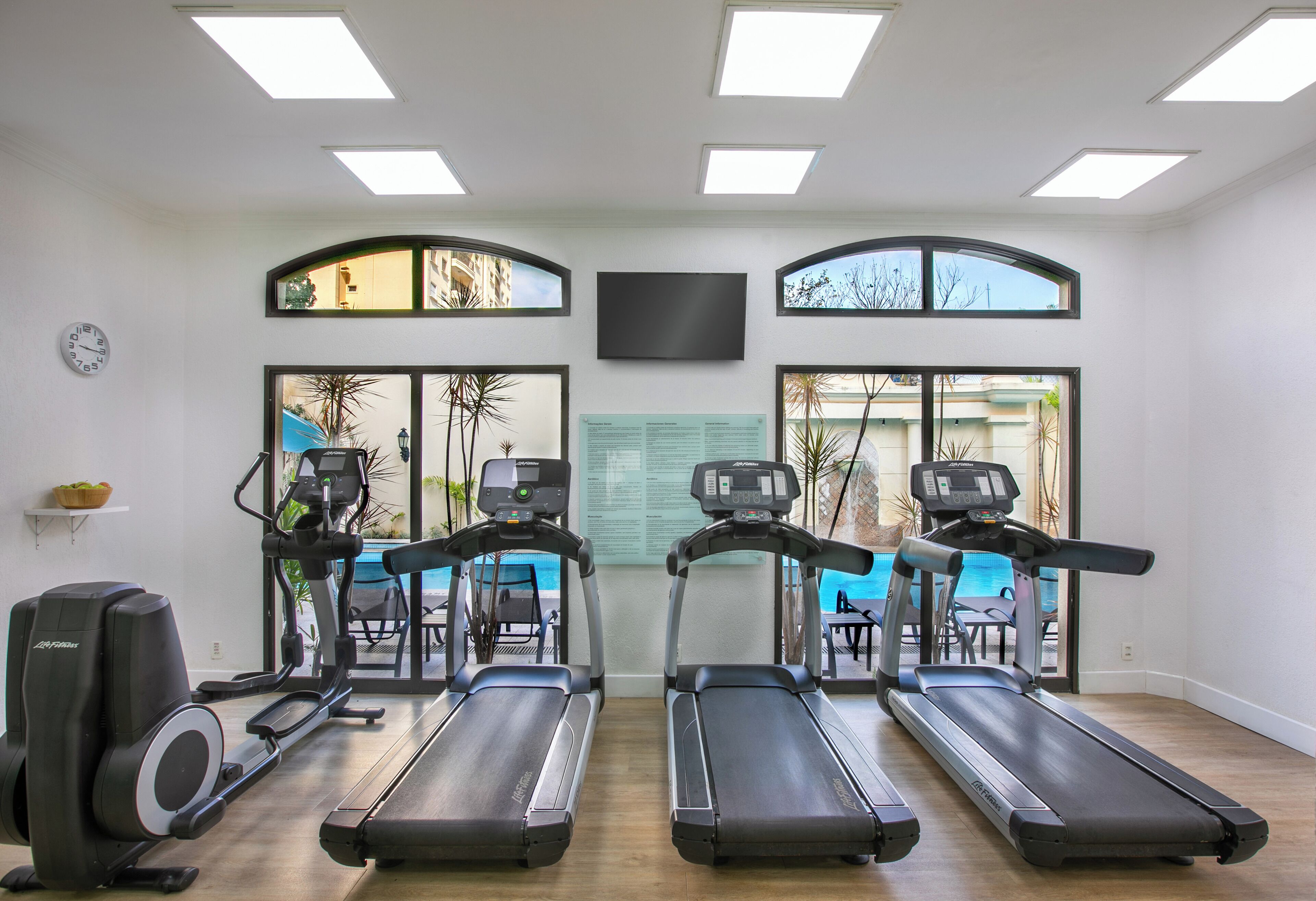 A gym with treadmills, a stationary bike, and a rowing machine. There are large windows with views of the outside.