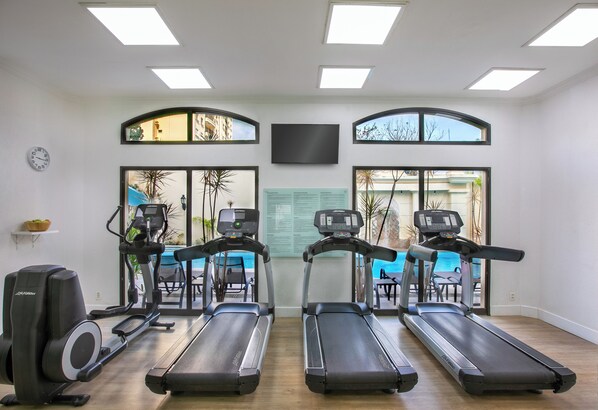 A gym with treadmills, a stationary bike, and a rowing machine. There are large windows with views of the outside. - Melia Campinas (Campinas)