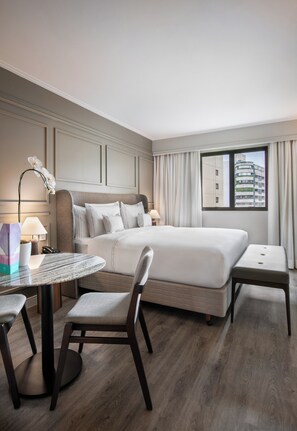 A hotel room with a bed, a round table, a chair, and a window with curtains.