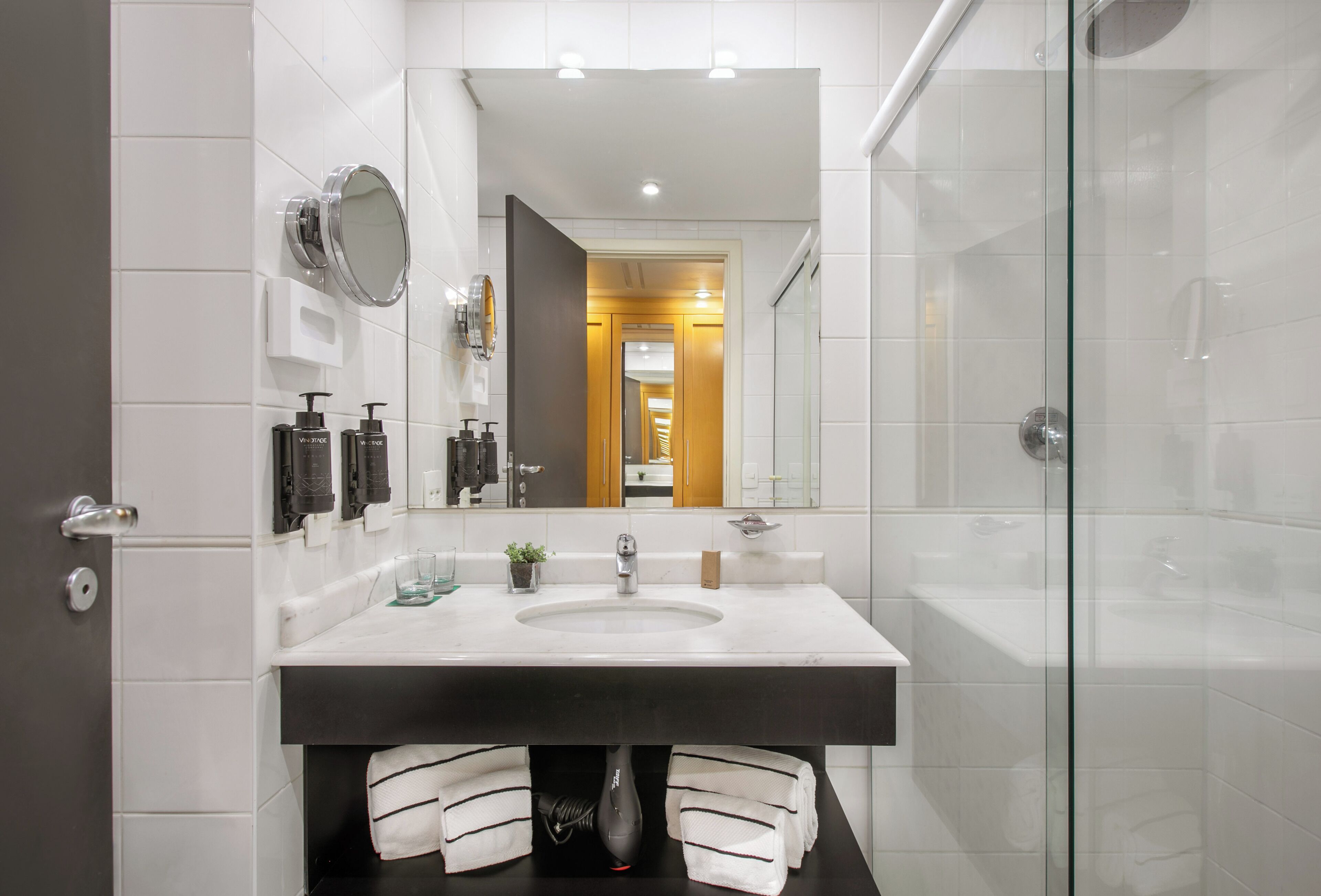 A modern bathroom with a large mirror, a sink, and a glass shower enclosure.