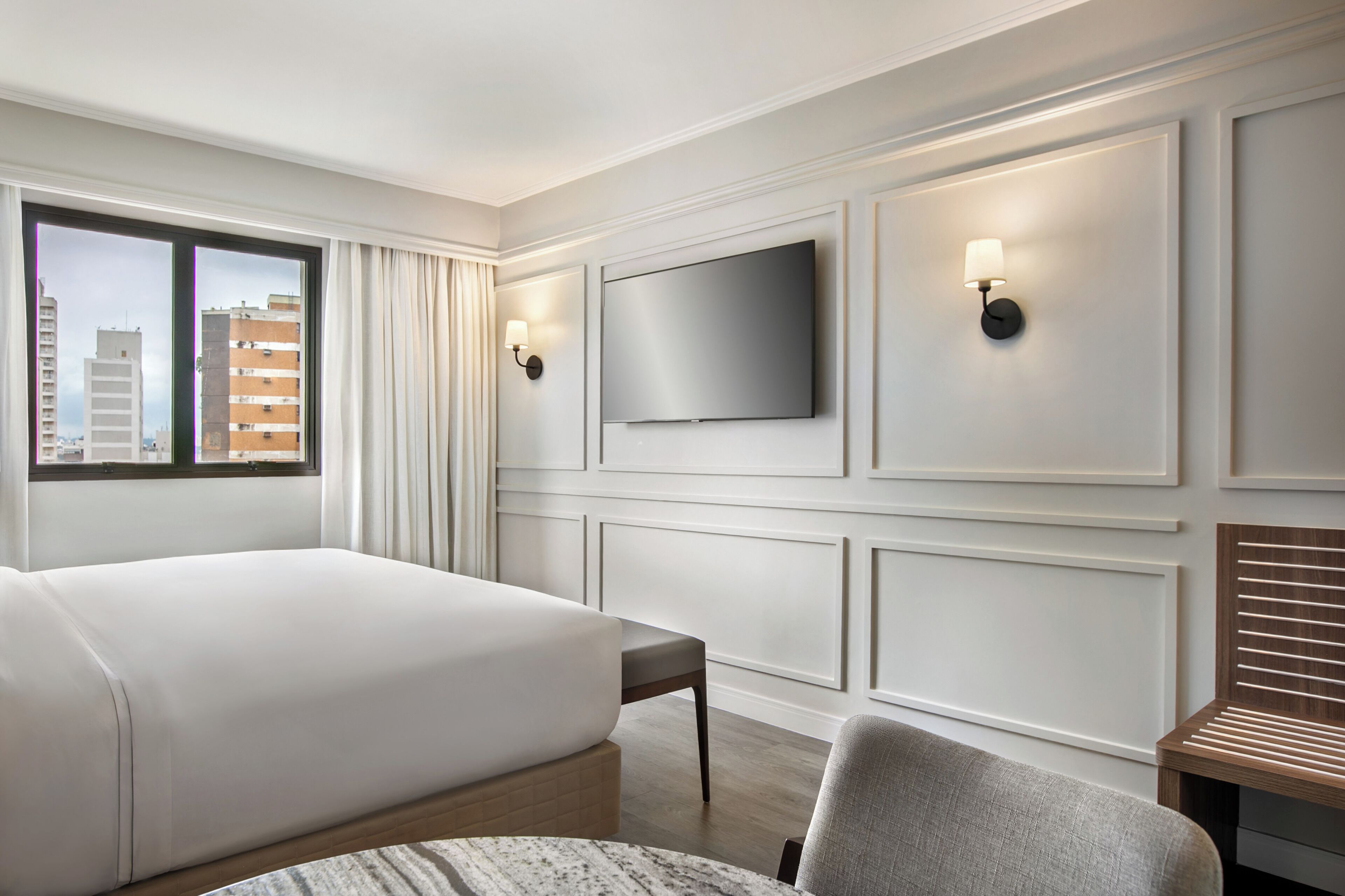 A hotel room with a large bed, a TV mounted on the wall, and a window with curtains.