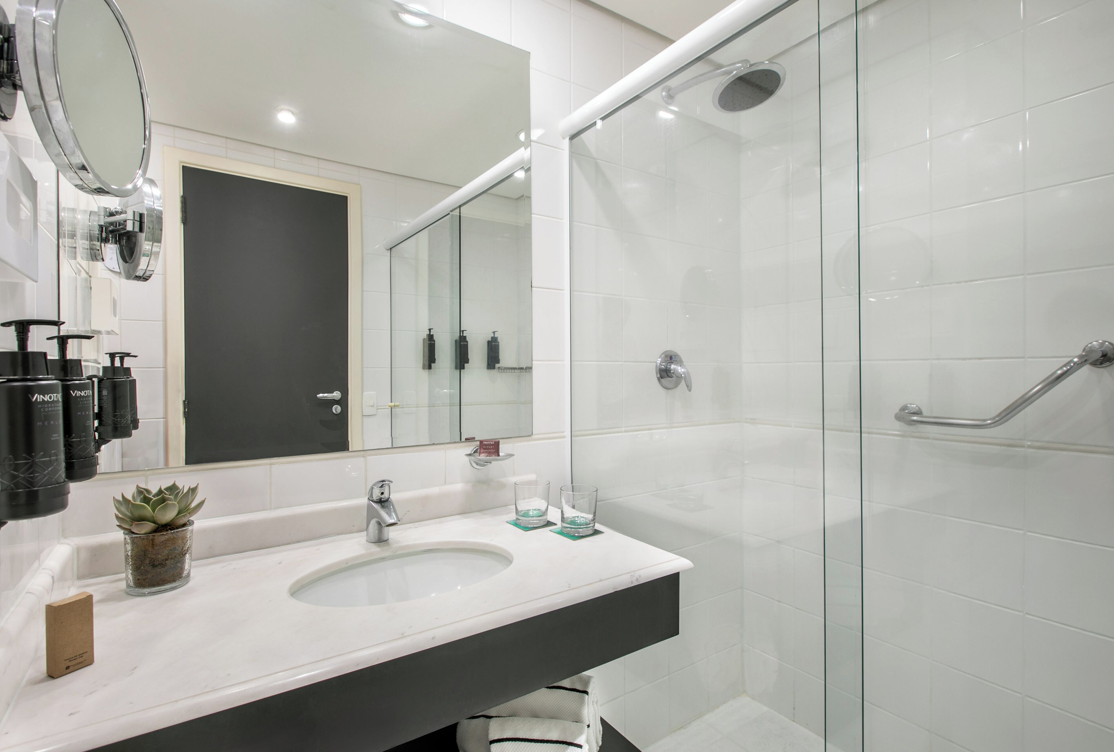 A modern bathroom with a white sink, a large mirror, and a glass-enclosed shower area.