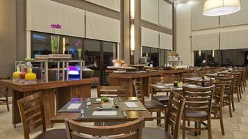 A spacious restaurant with multiple dining tables and chairs, a bar area, and a large window with decorative plants.