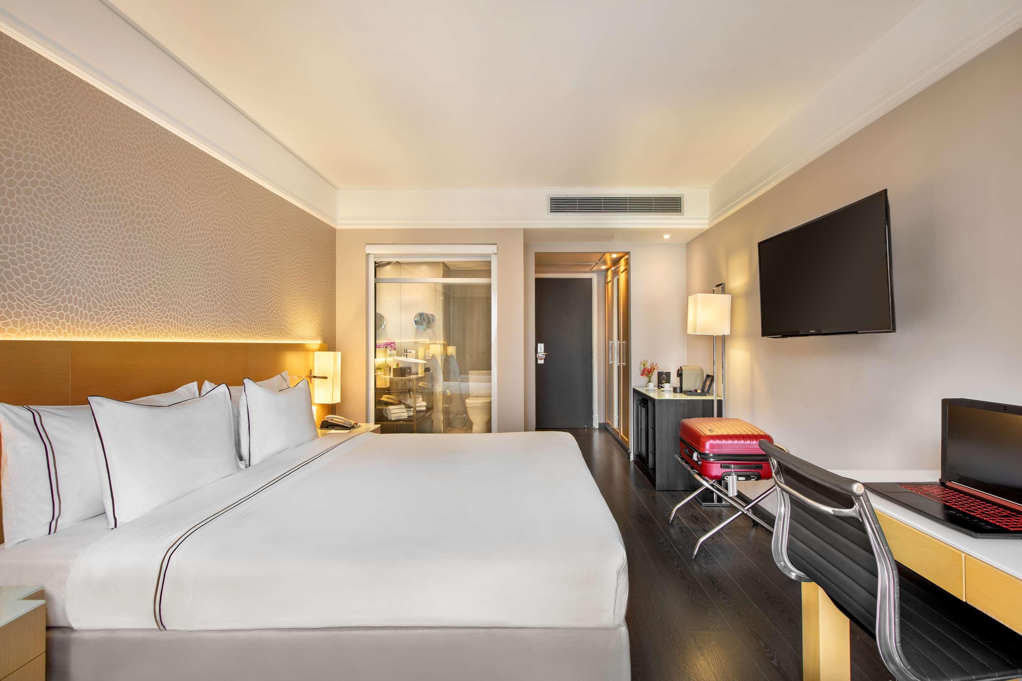 Hotellihuone, jossa on suuri sänky, työpöytä kannettavalla tietokoneella, televisio ja matkalaukku.